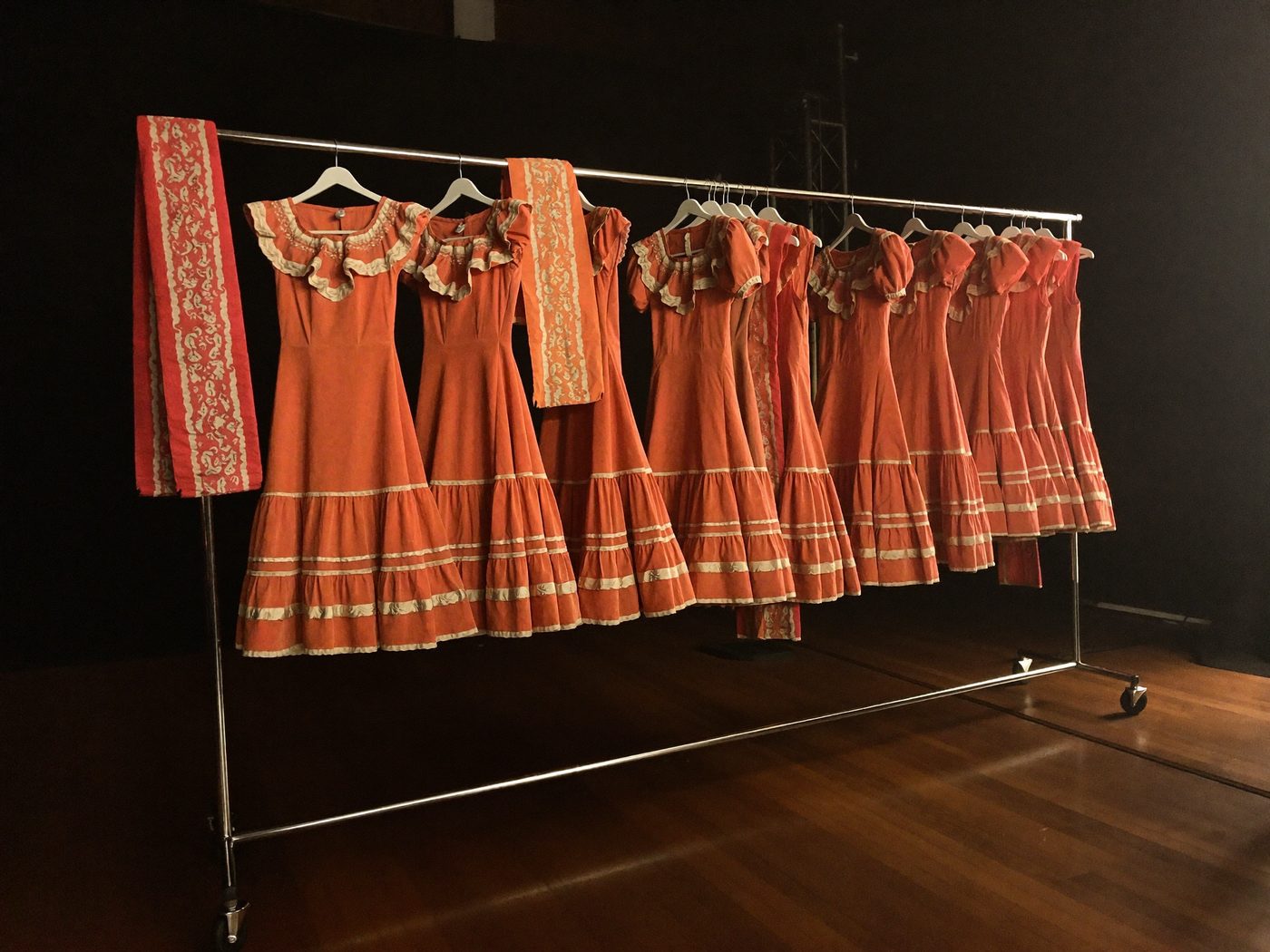 A backstage wardrobe rack holding a matching set of coral folklorico dresses for a dance group